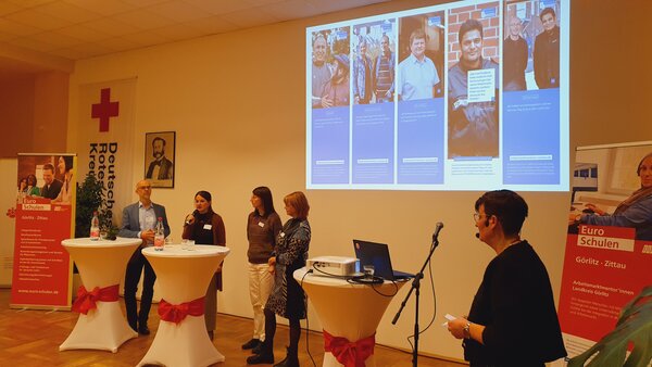 Menschen erfolgreich in Arbeit oder Ausbildung begleiten Teilnehmende tauschen sich an Stehtischen aus und zeigen Erfolge per Beamer in einer Präsentation.