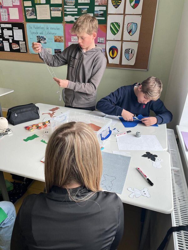 „Praxisberater*innen an Oberschulen“ – Potentialanalyse Drei Schüler*innen arbeiten an einem Bastelprojekt. Ein Junge entwirrt Wolle, ein anderer schneidet aus Filz, während auf dem Tisch Tierfiguren und Bastelmaterialien liegen.