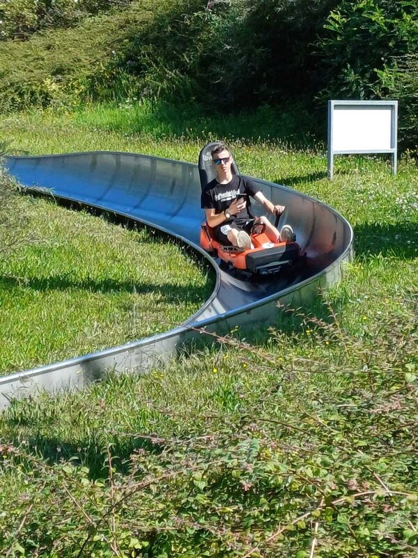 Abschlussfahrt: Erlebnispark Teichland Ein junger Mann mit reflektierender Sonnenbrille bremst mit einer Hand das Gefährt einer Sommerrodelbahn. In der anderen Hand hält er ein Handy.