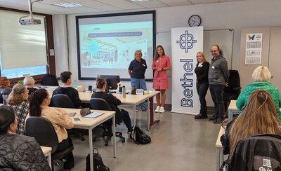 In einem Klassenraum sitzen viele Schülerinnen und Schüler die einer Präsentation zuhören.