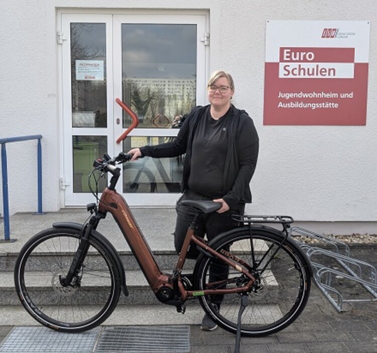 Freude über das Fahrrad-Leasing: Eine Erfolgsgeschichte Mitarbeiterin Lisa posiert vor dem Eingang der Euro-Schulen Hoyerswerda mit ihrem neuen Fahrrad.