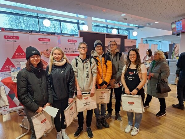 Erfolgreicher Messebesuch Die Teilnehmenden stehen mit Tüten mit Werbegeschenken gut gelaunt in den Räumen der Jobmesse und posieren für ein Gruppenbild.