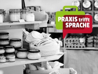Praxis trifft Sprache - Einzelhandel Ein Regal in einem Laden zeigt verschiedene Produkte wie Gläser mit Cremes, eingemachte Gläser und gefaltete Handtücher in Körben. Im Vordergrund ist eine grüne Sprechblase mit der Aufschrift 'PRAXIS trifft SPRACHE' in weißer und roter Schrift eingeblendet. Der Hintergrund des Bildes ist in Schwarz-Weiß gehalten, während die Sprechblase farbig hervorgehoben ist.