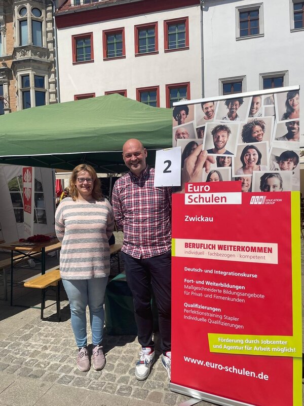 Interkulturelles Familienfest Zwikkolör Mitarbeitende der Euro-Schulen Zwickau posieren lächelnd für ein gemeinsames Bild vor ihrem Euro-Schulen Infostand auf dem Interkulturellen Familienfest in Zwickau.