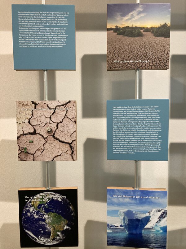 Exkursion ins Stadtmuseum Jena Eine Wandinstallation mit mehreren Informationstafeln und Bildern, die sich mit verschiedenen Aspekten des Wasserkreislaufs und der Wasserknappheit beschäftigen. Die Texte erklären Themen wie Verdunstung, die Veränderung der Wassermenge auf der Erde und die Bedeutung von Süßwasser.