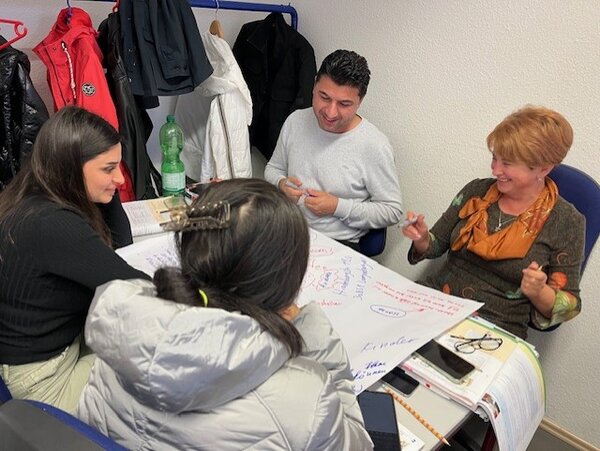 Erfolgreiche Gruppenarbeit im Berufssprachkurs Vier Teilnehmende eines Berufssprachkurses lachen bei der gemeinsamen Arbeit.