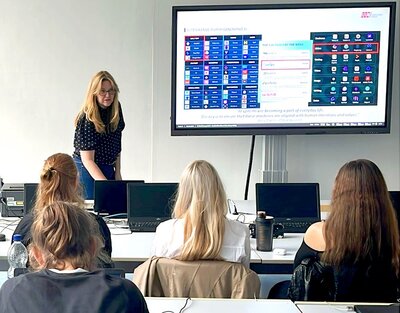 Vortrag zu KI Workshopleiterin steht vorn im Klassenraum und referiert vor Schülerinnen und Schülern über Künstliche Intelligenz.