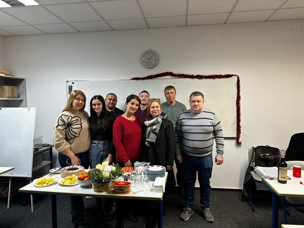 Weihnachtsfeiern in Köln Die Kursteilnehmenden stehen in ihrem Klassenzimmer und präsentieren die mitgebrachten Leckereien.