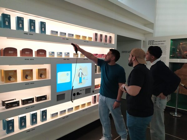 Sonniger Exkursionstag der Euro-Schulen Dresden: Spannende Einblicke in Wissenschaft und Kultur Drei Personen stehen vor einem interaktiven Display in einer Ausstellung über Ernährung. Eine Person benutzt einen Scanner, um Informationen zu verschiedenen Lebensmitteln aufzurufen.