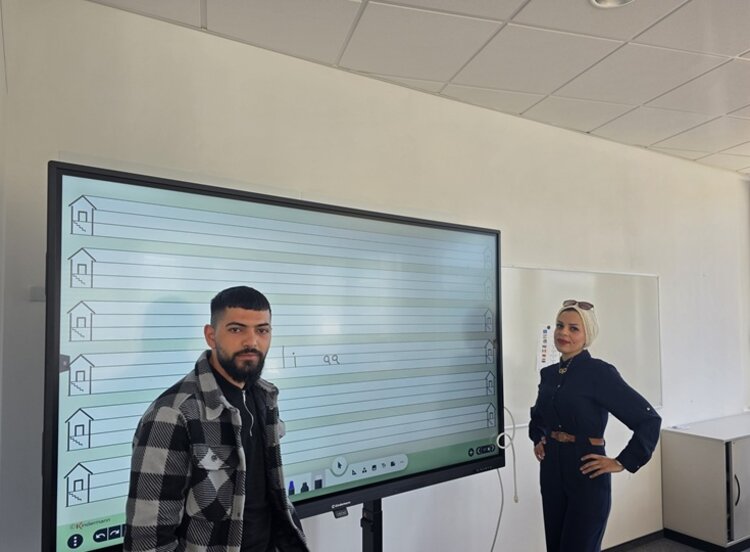 Vom Sprachkurs ins Berufsleben Ein männlicher Teilnehmer des Integrationskurses an den Euro-Schulen Dresden steht, gemeinsam mit der ehemaligen Teilnehmerin, die als Gast den Kurs besuchte, im Unterrichtsraum vor dem großen interaktiven Whiteboard.