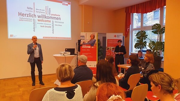 Menschen erfolgreich in Arbeit oder Ausbildung begleiten Teilnehmende im Saal, hören einen Vortrag, der Beamer projiziert herzlich willkommen an die Wand.