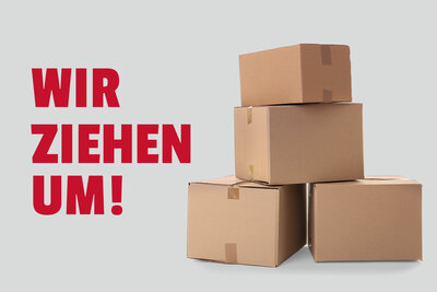 Im linken Bereich des Bildes ist die Aufschrift "Wir ziehen um!" in roten Lettern, im rechten ein Stapel mit Umzugskartons zu sehen. Der Hintergrund ist grau. 