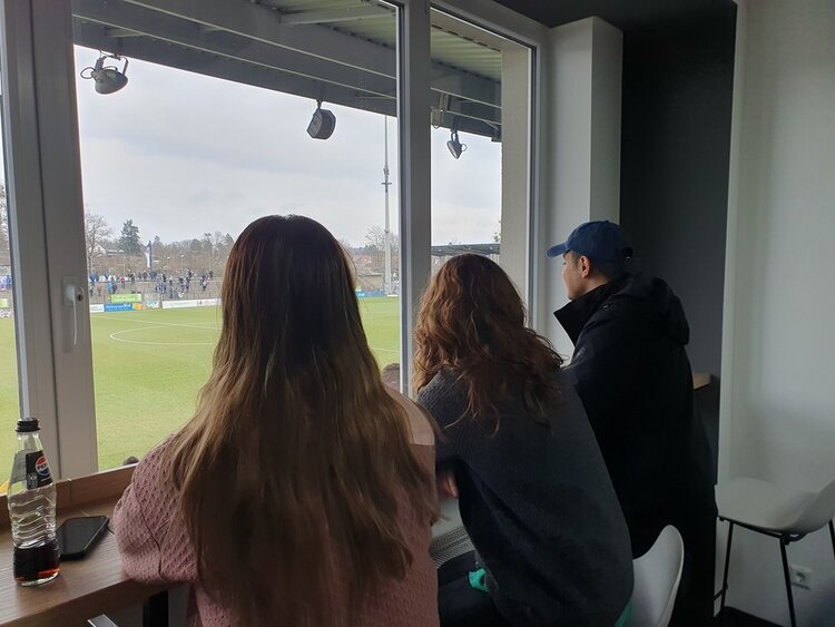 Stadionerlebnis der Extraklasse bei Turbine Potsdam Zwei Frauen und ein Mann schauen aus der VIP-Lounge durch ein großes Fenster auf das Geschehen auf dem Spielfeld.