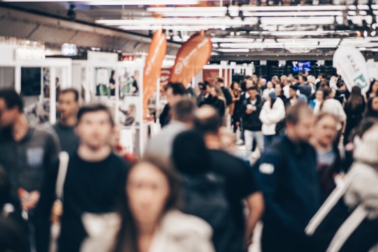 Besuch der Jobmesse in Leipzig In einer Messehalle tummeln sich die Besucherinnen und Besucher in den Gängen. Die Gesichter der Menschen sind verschwommen und nicht erkennbar.