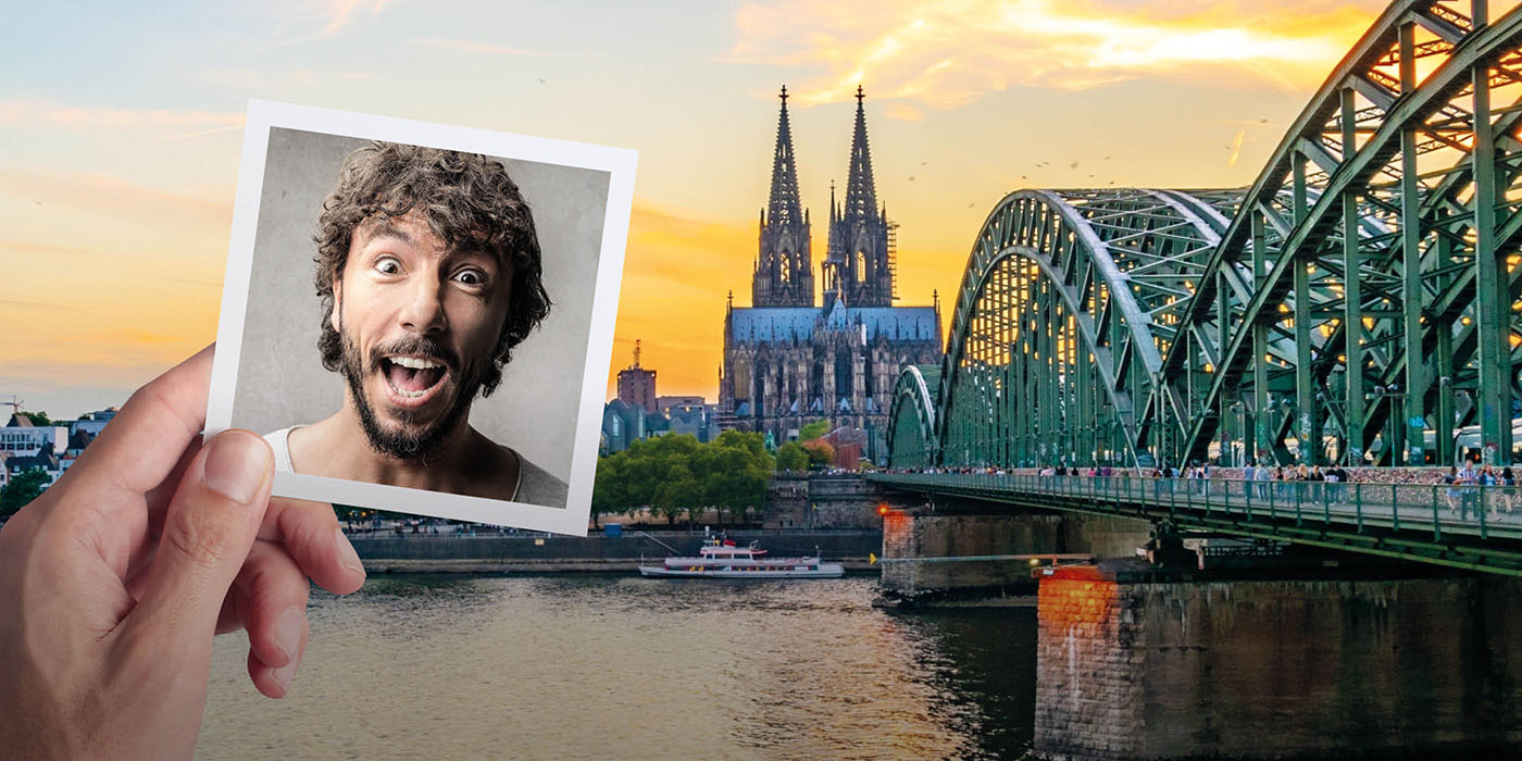 Eine Hand hält ein Foto von dem Gesicht einer überrascht schauenden Person vor eine malerische Ansicht auf den Dom von Köln und der Hohenzollernbrücke, die über den Rhein führt. Die Sonne geht gerade unter und alles ist in ein goldgelbes Licht getaucht.